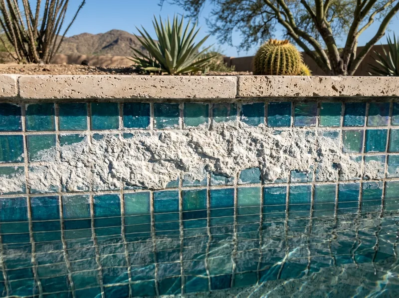 Chalky white calcium scale banded across the glass mosaic waterline tiles of a pool, with clean tile visible below the line.
